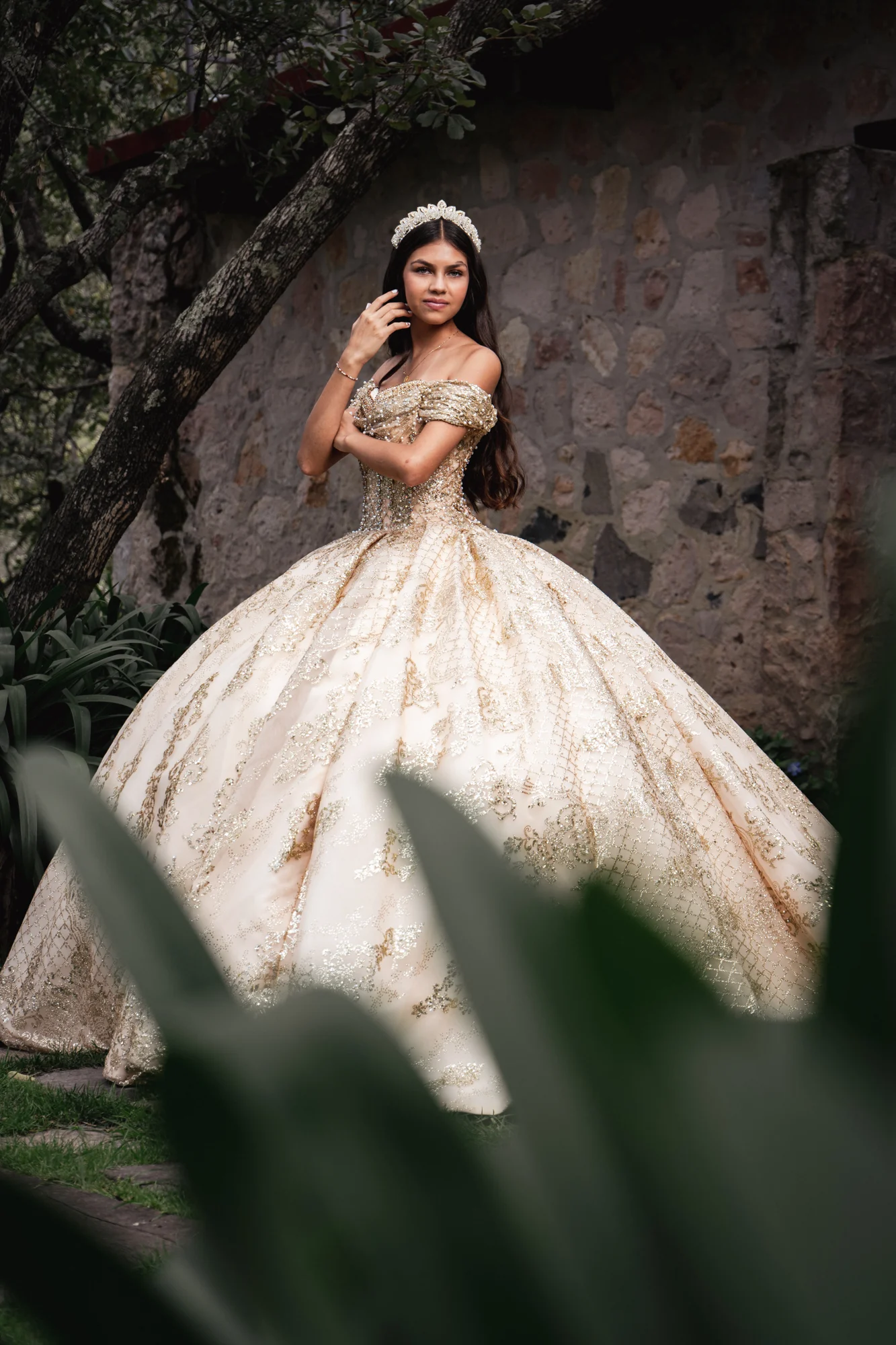 Quinceañera con vestido dorado entre árboles
