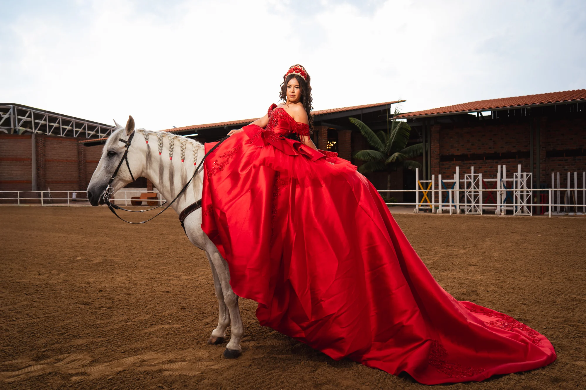 Quinceañera con vestido rojo sobre un caballo blanco