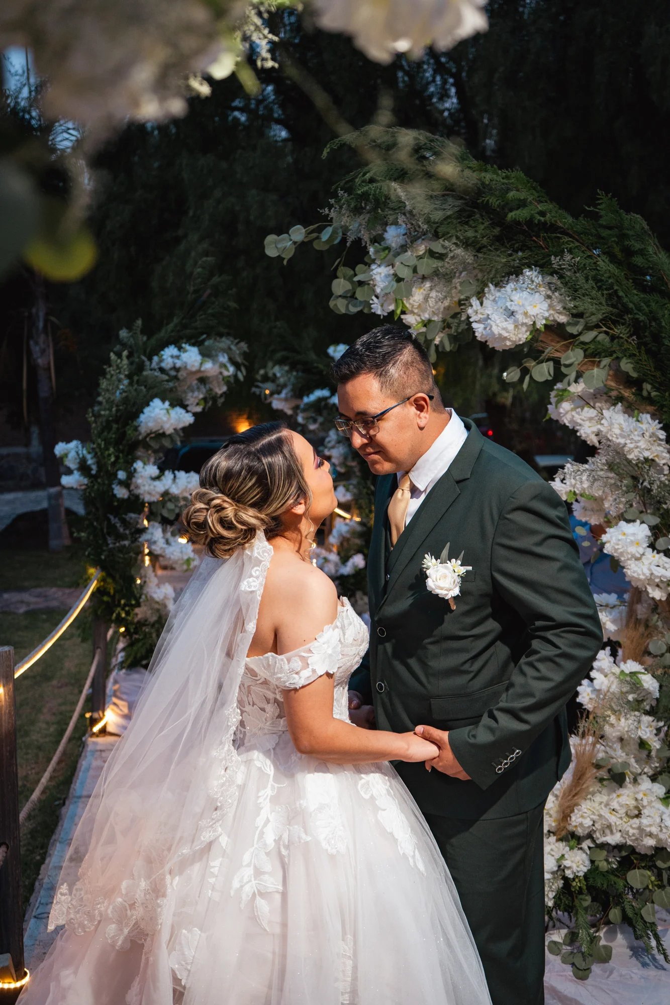 Novios tomados de la mano bajo un arco floral
