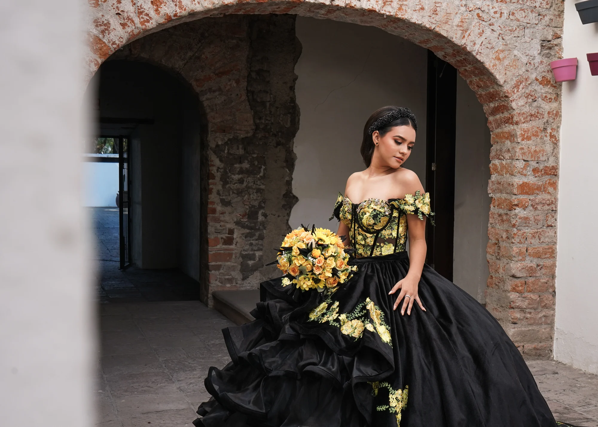 Quinceañera con vestido negro y bordados amarillos bajo un arco