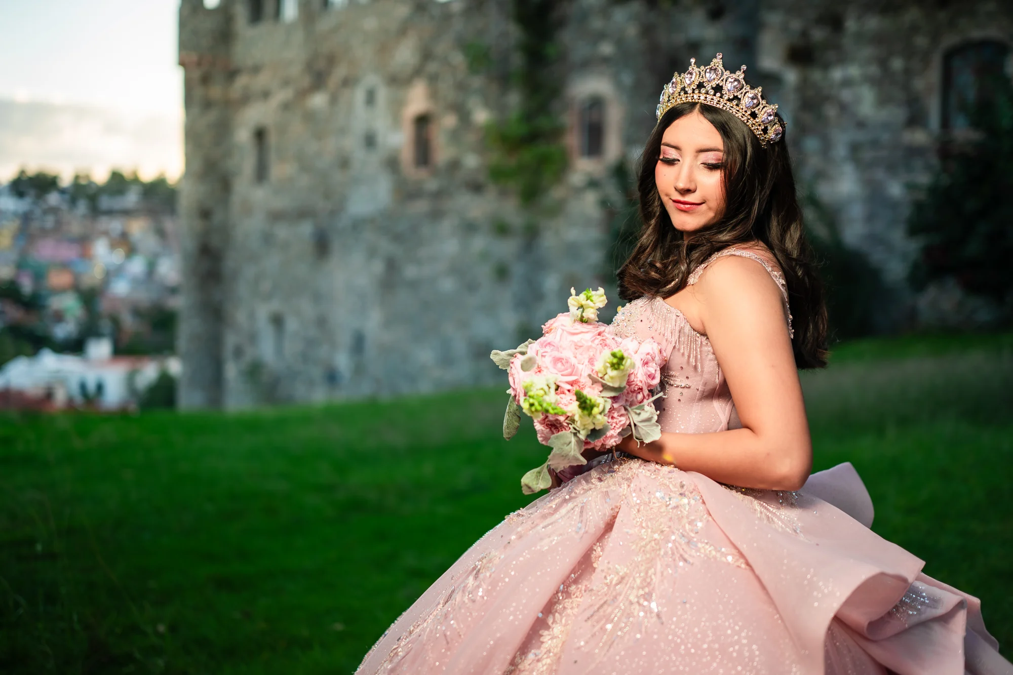 Quinceañera de rosa con corona y ramo frente al castillo