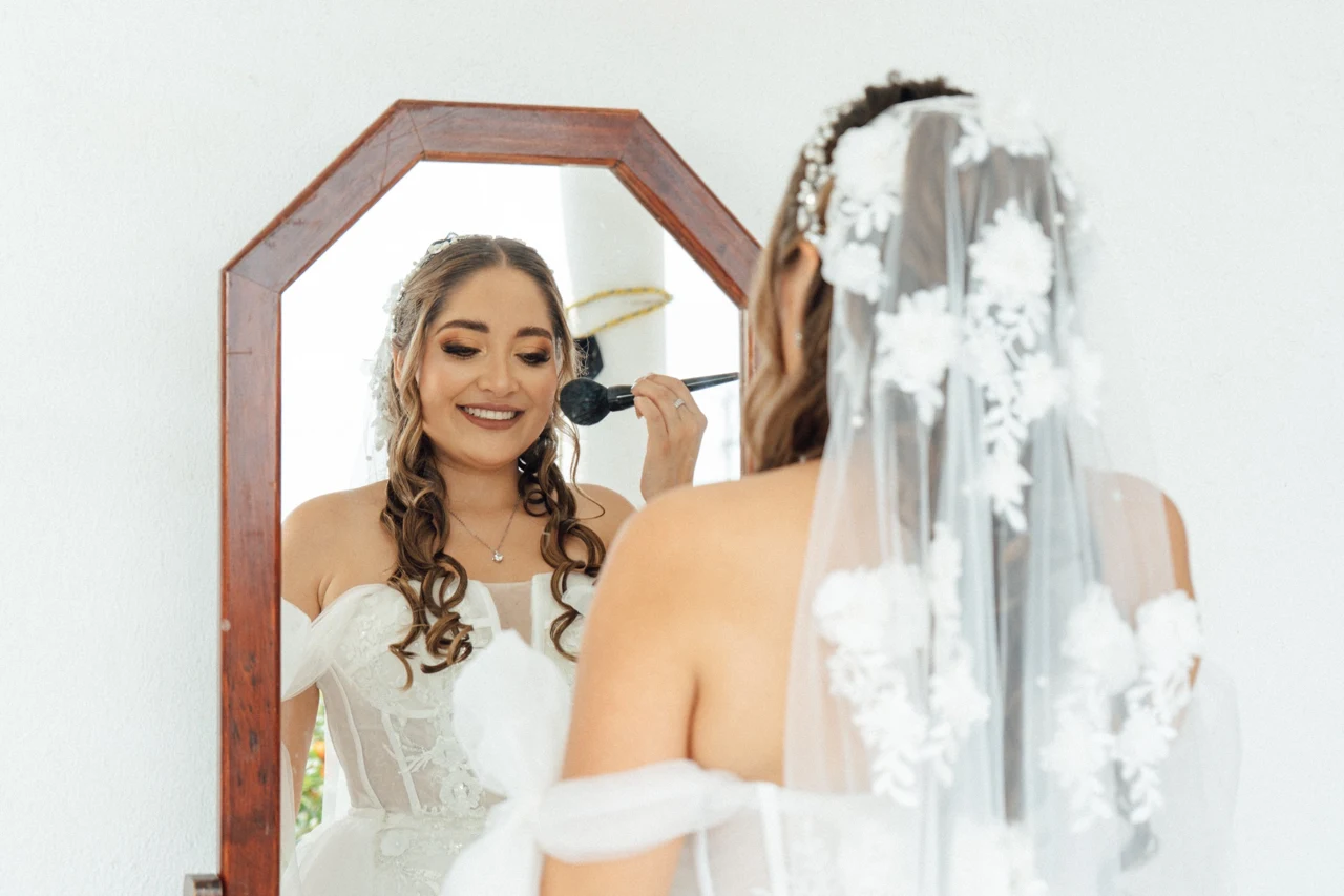 La novia retoca su maquillaje frente al espejo, con el velo puesto