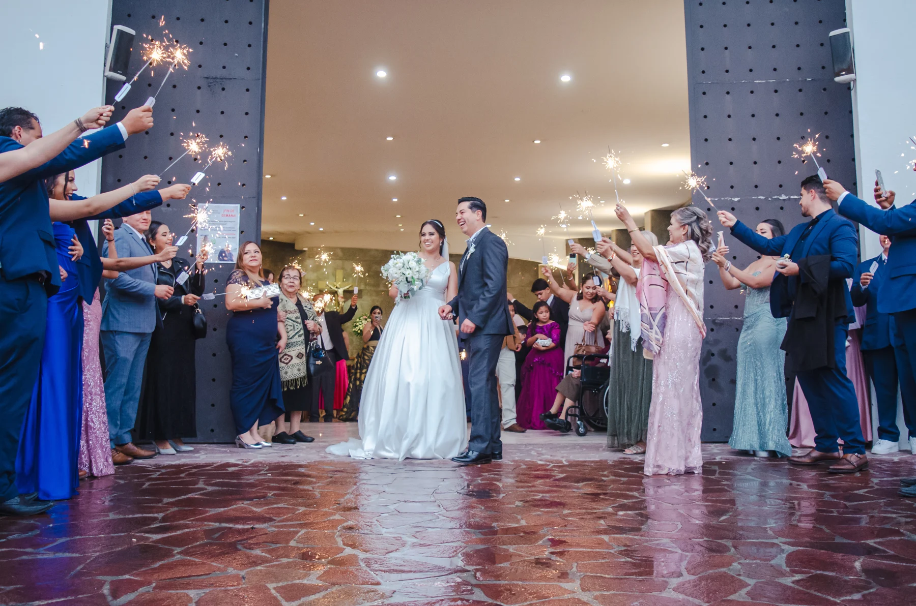 Los novios a la salida del templo, rodeados de invitados con luces de bengala