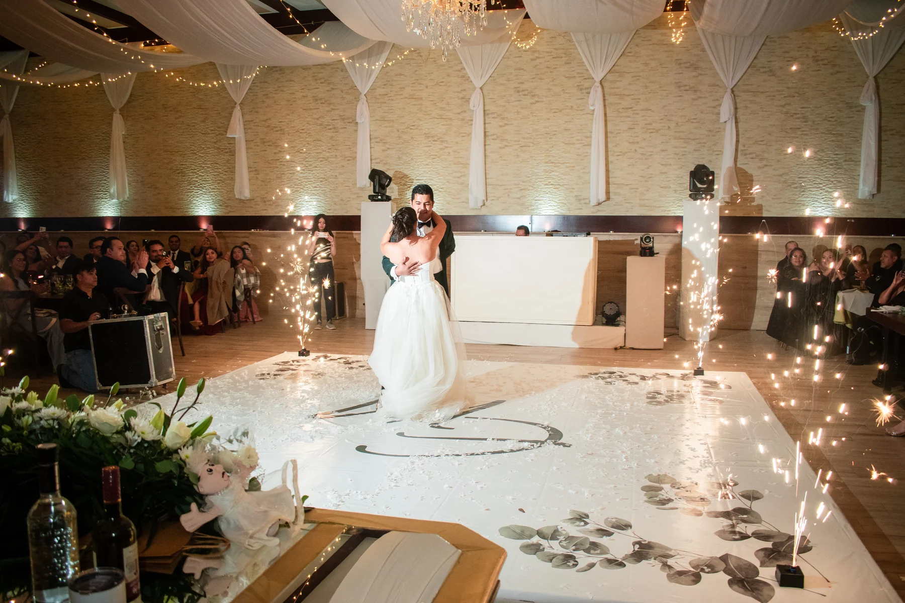 Los novios disfrutan su vals en la pista, rodeados de invitados y luces de bengala